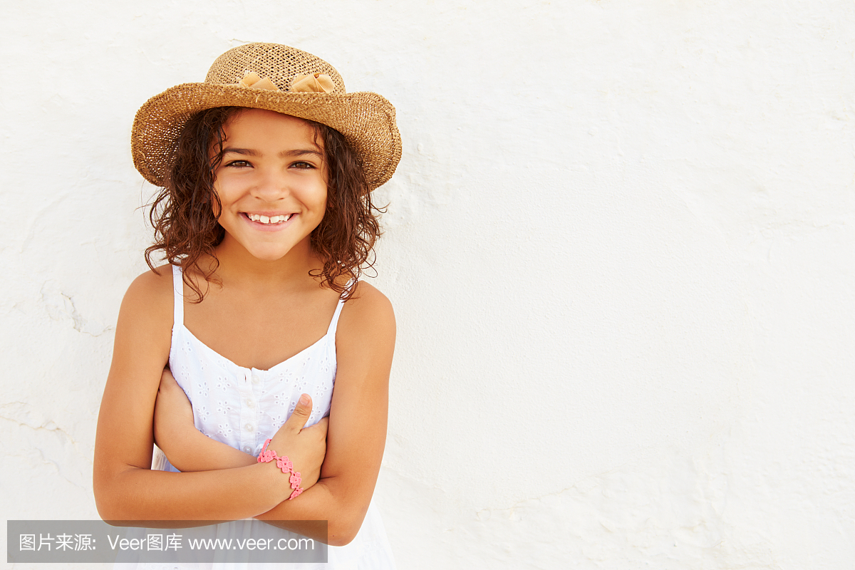 微笑的小孩戴着帽子反对白墙