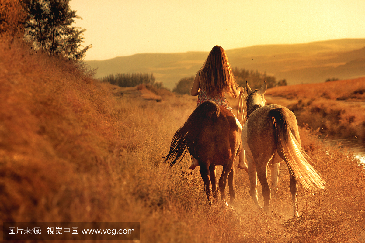 女孩在日落时骑着马向农村的小山走去