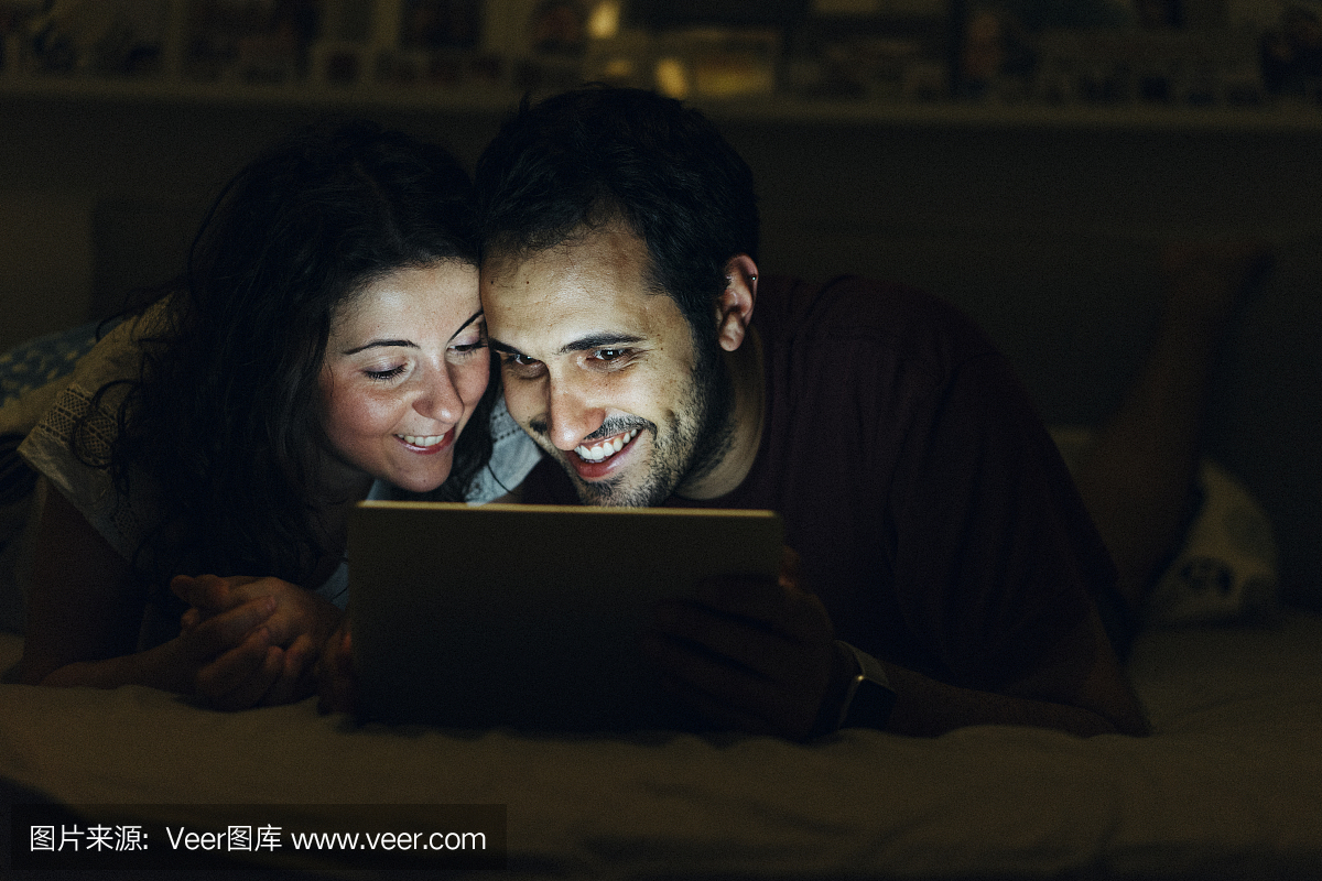年轻的成年夫妇在床上一起浏览网