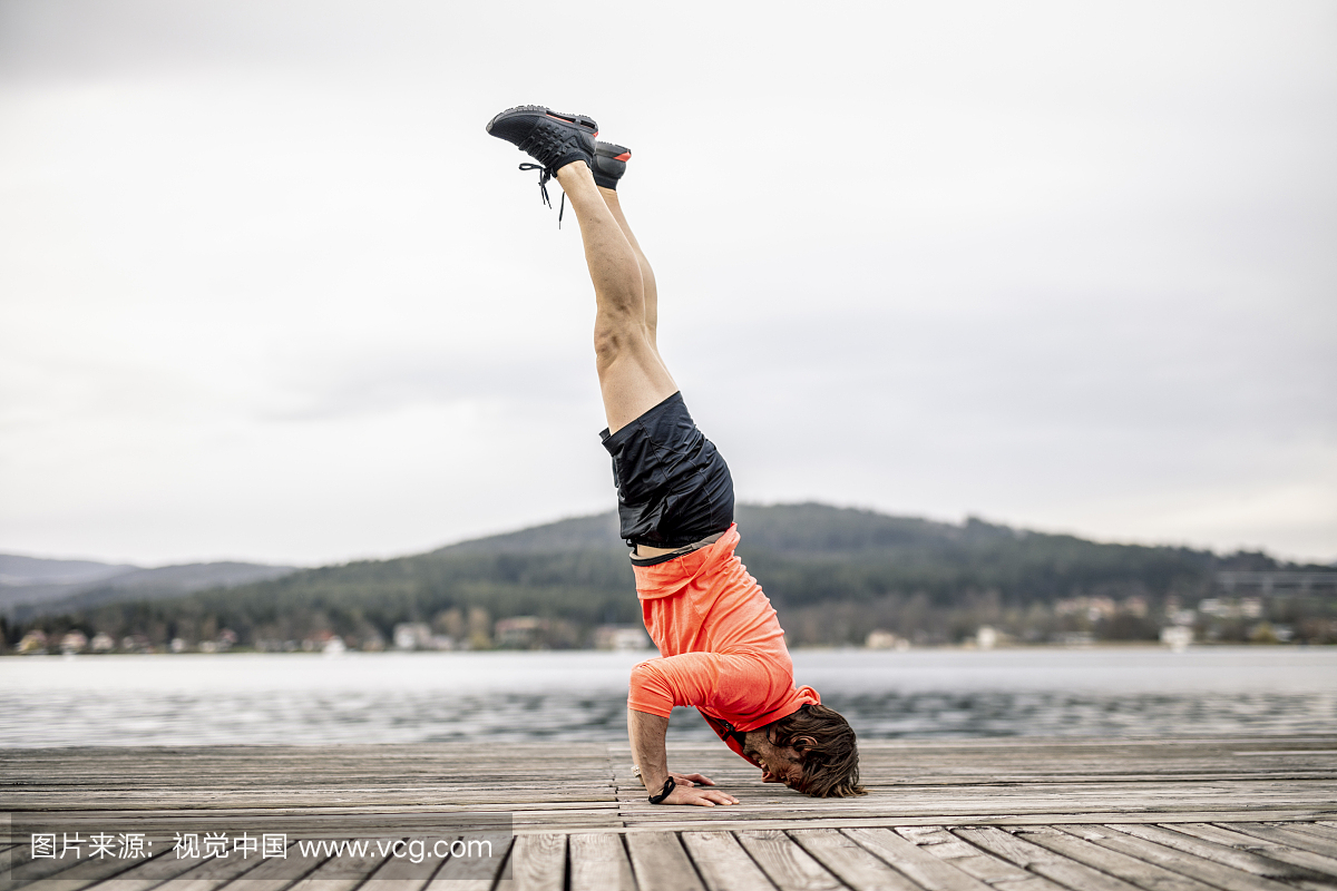 Athlete doing a headstand on wooden deck at t