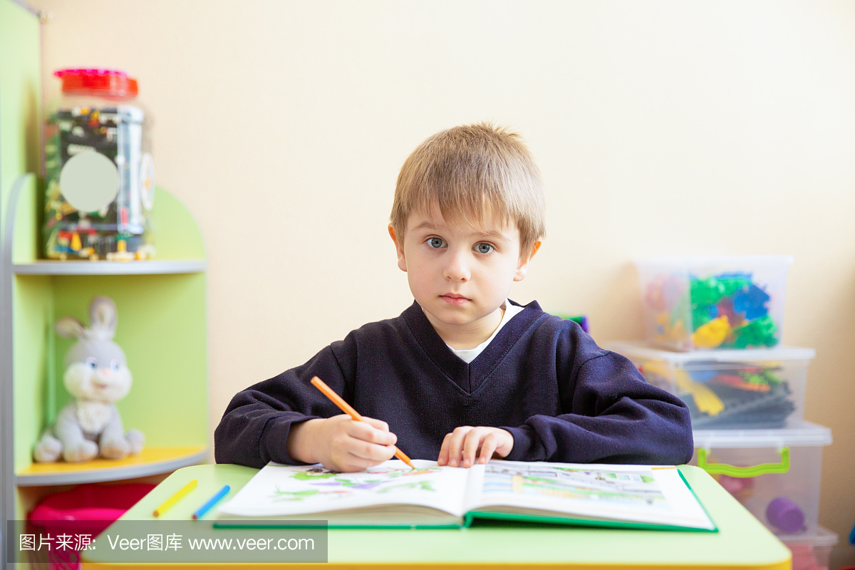 可爱的男孩与素描笔和书在教室里桌子上的肖像