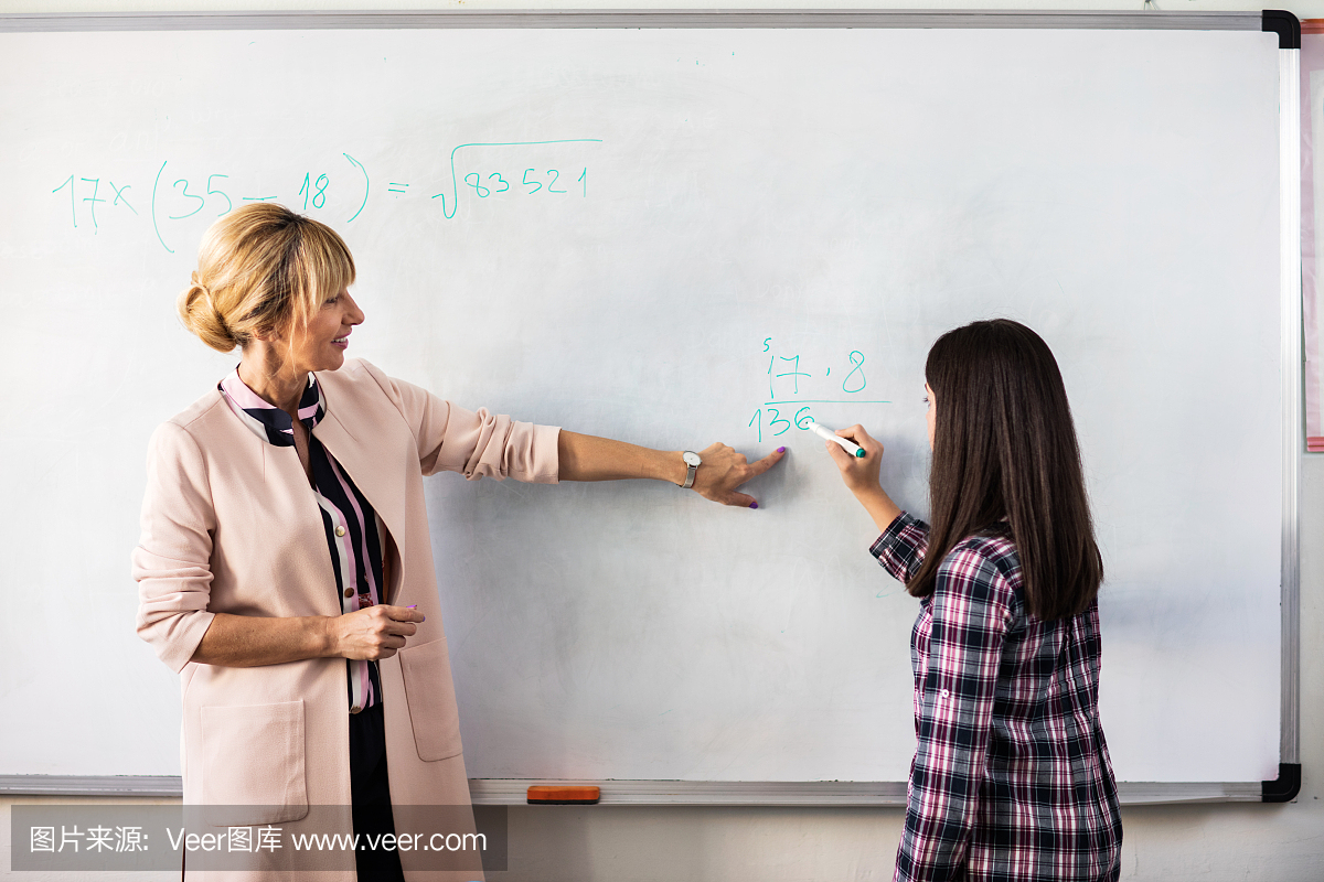 老师帮助女学生解决白板上的数学公式。