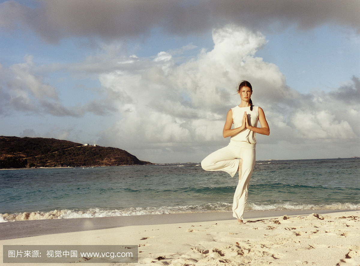 做瑜伽姿势的年轻女子在海滩上