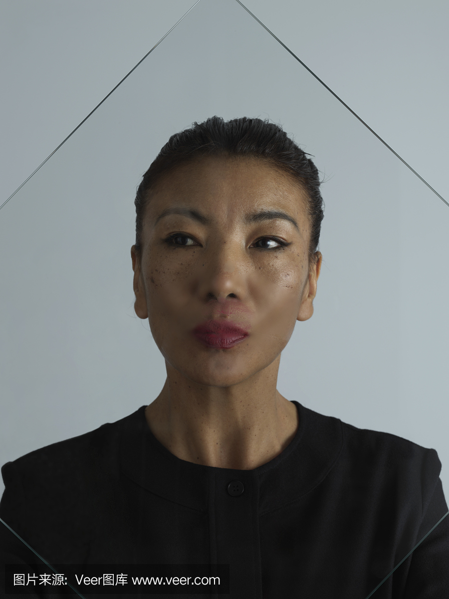 老年女性对平原灰色背景亲吻玻璃的爆头