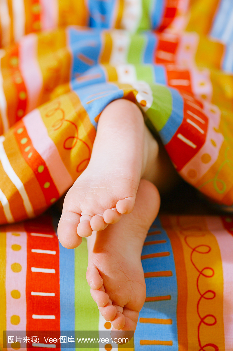 幼儿女孩的脚在早晨的阳光下的床上