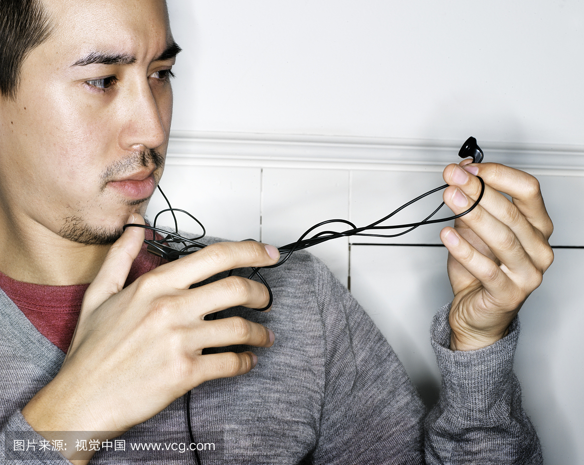 年轻亚洲男用扭曲耳机电缆