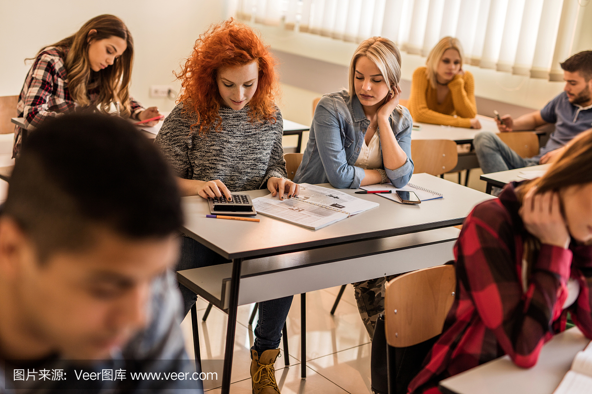 红头发学生使用计算器和在教室里学习。