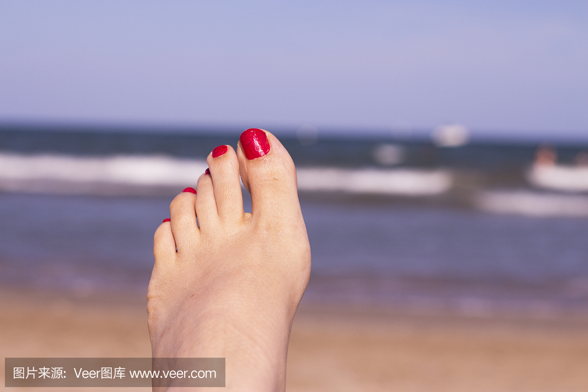海滩场面与女人的脚在沙滩上。脚指甲红色