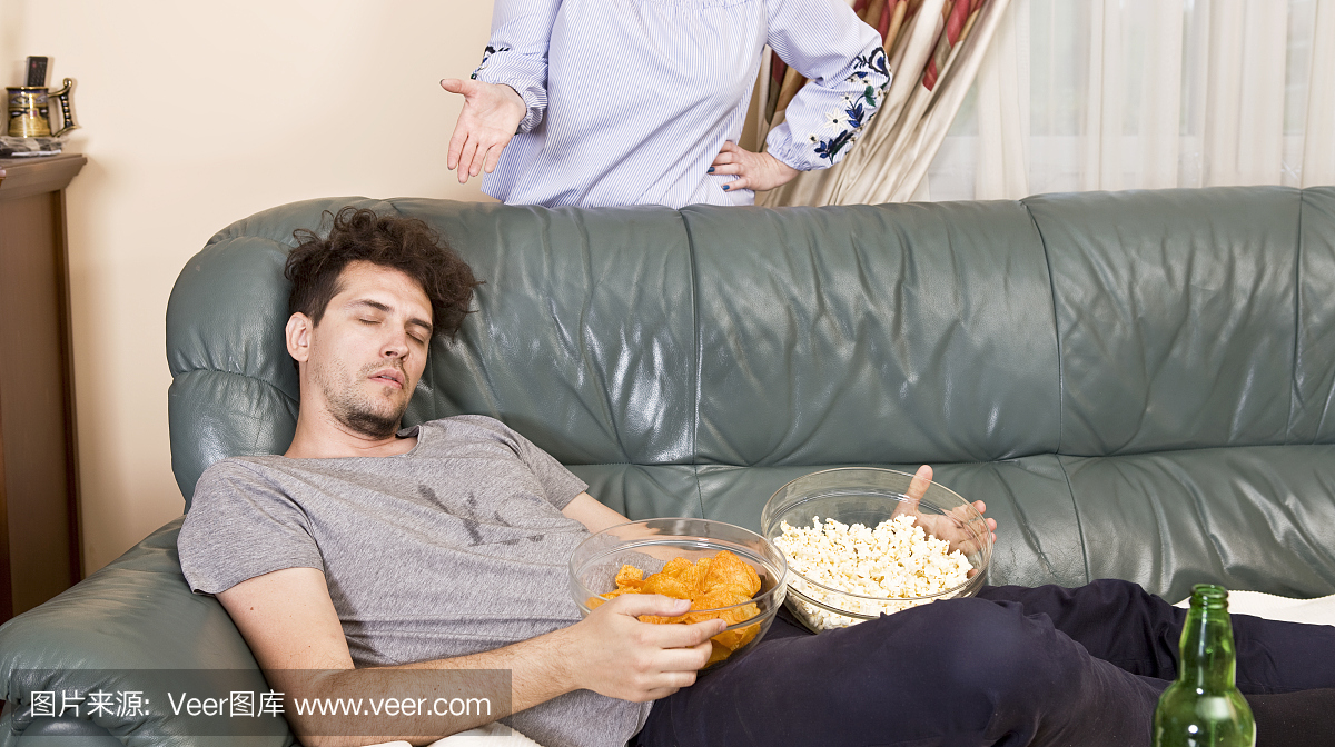 生气的妻子和睡觉的丈夫在沙发上和垃圾食品