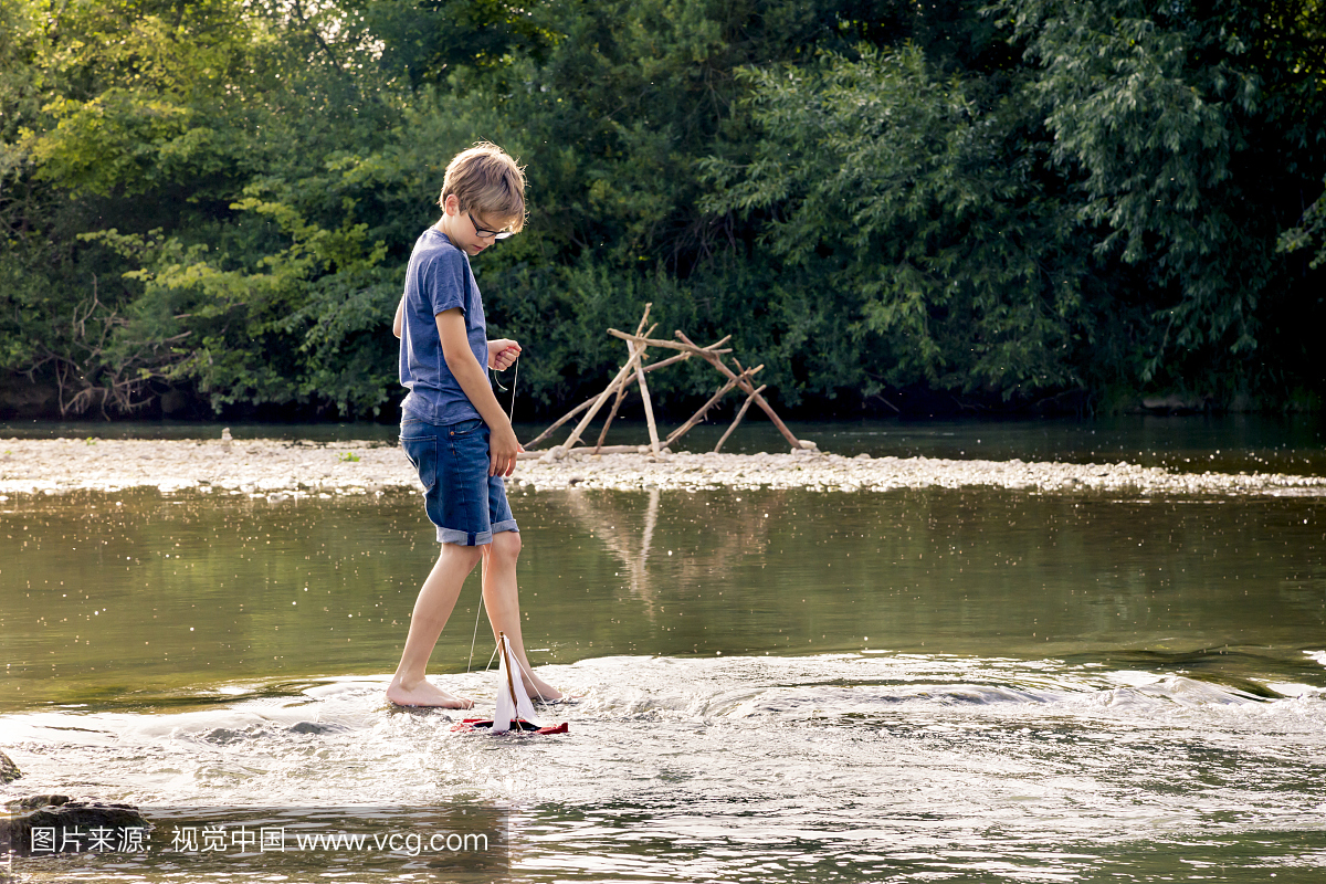 男孩玩在一条河上的木玩具船