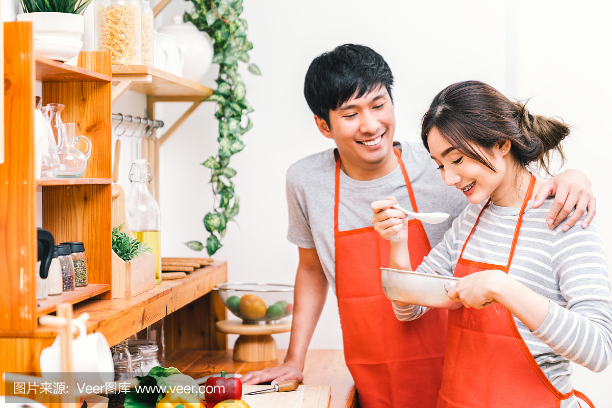 年轻的亚洲可爱的夫妇在家里一起做饭厨房,穿
