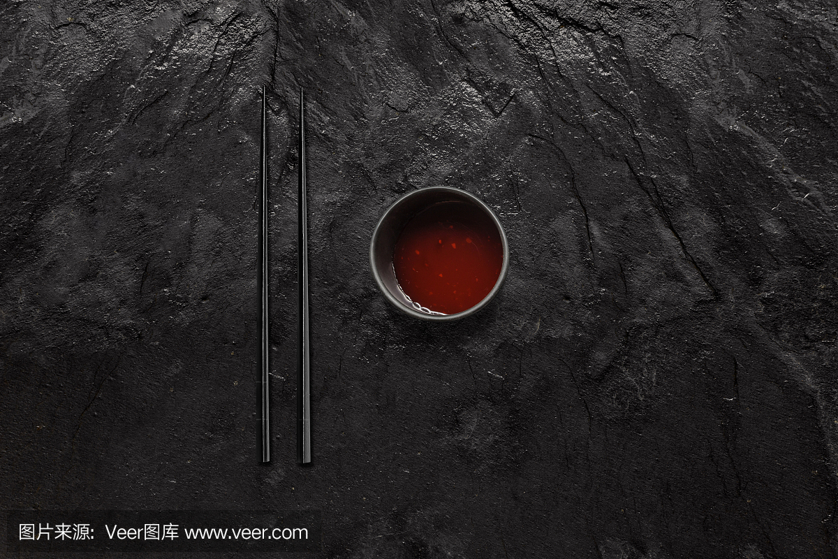 黑筷子和黑醋栗石头上的糖醋酱碗。