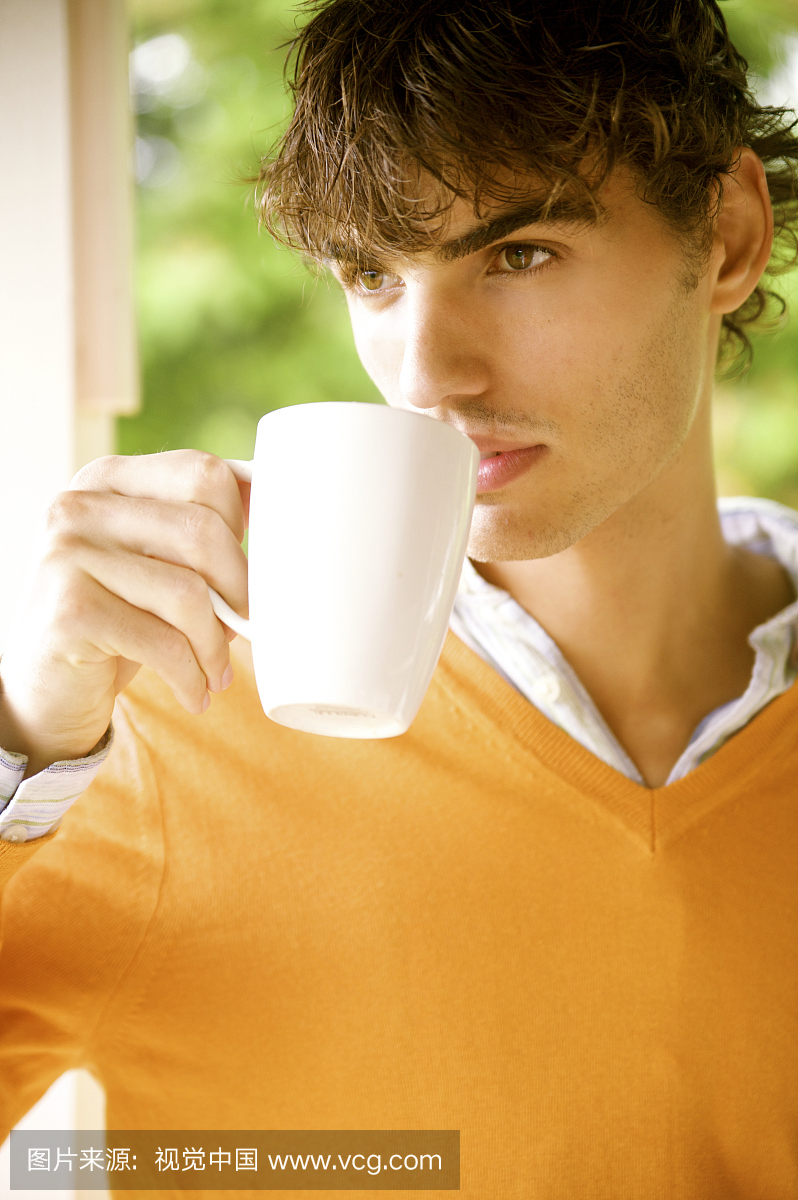 夏威夷,橙色毛衣喝咖啡的欧洲男模特肖像。