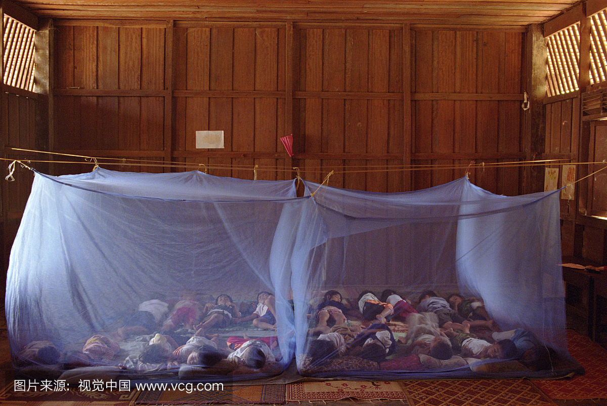 老挝,在日托工作场所睡在蚊帐下的孩子