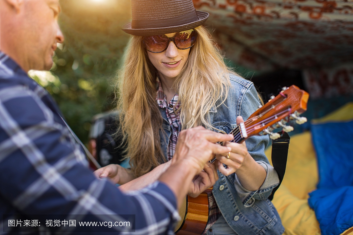 成熟的男人显示女朋友如何玩ukulele,同时露营