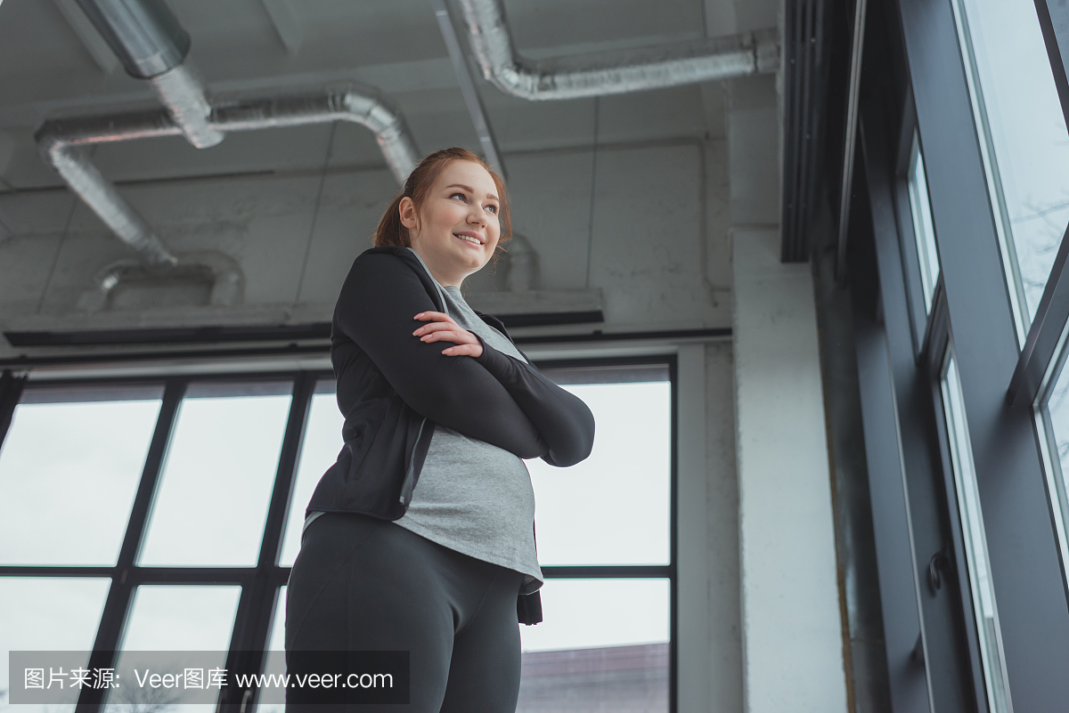 运动服站在窗户在健身房的肥胖女孩