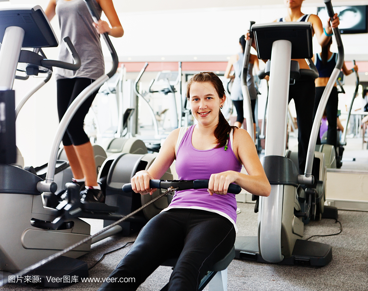 在健身房使用划船机的微笑的年轻女子