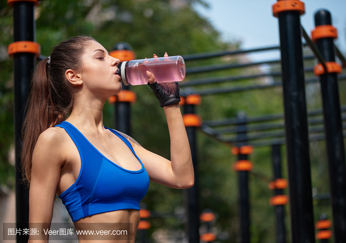 体育女子在街头健身房喝维生素水