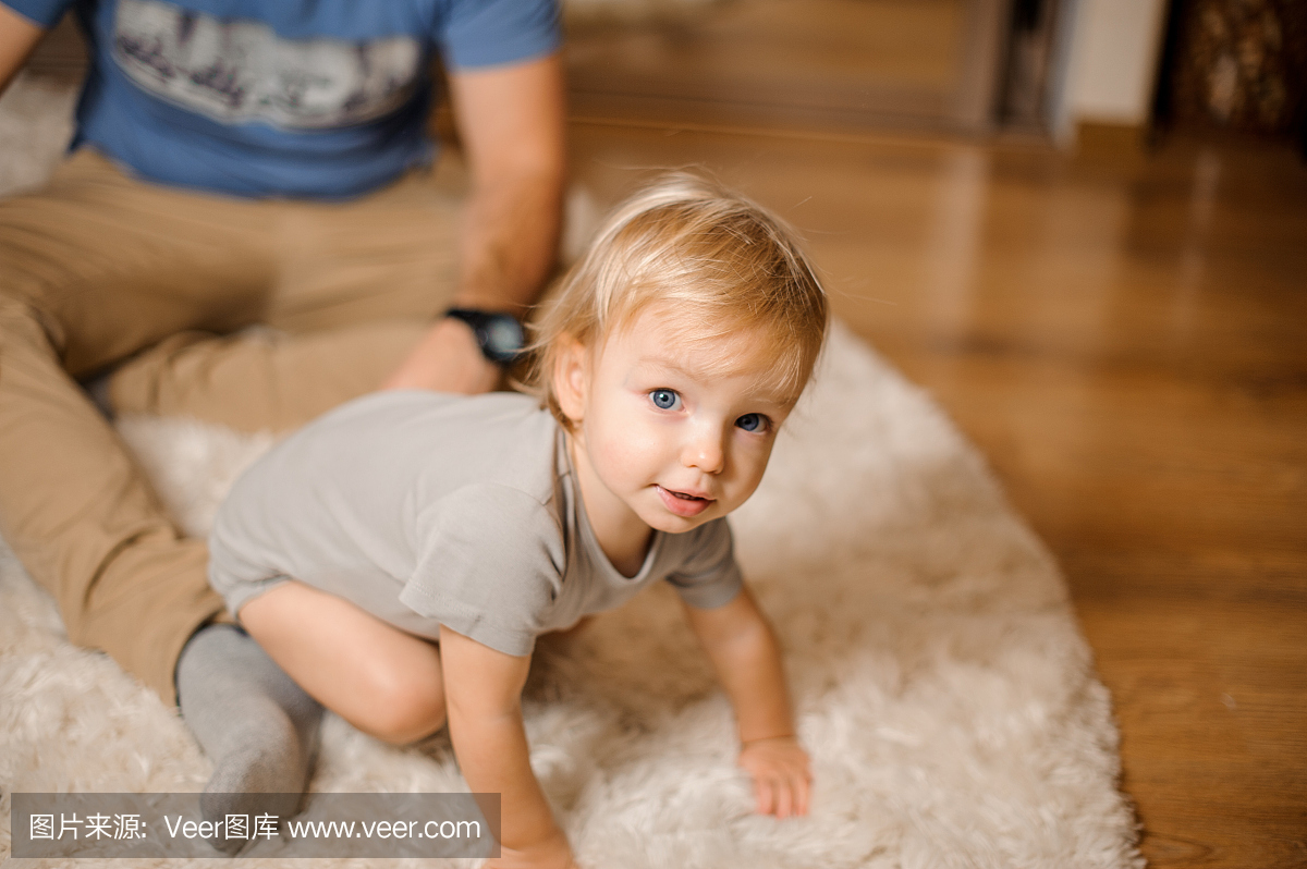 可爱的金发和蓝眼睛的婴儿穿着一件灰色的爬衣
