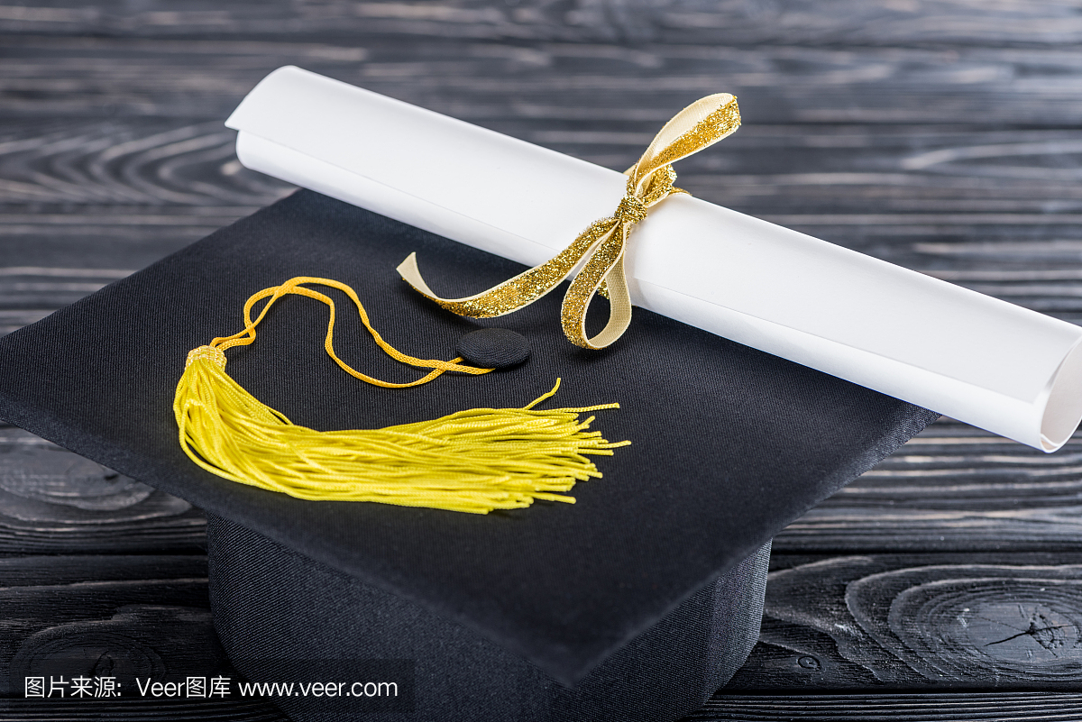 毕业帽子和文凭与木制的桌子上的黄丝带