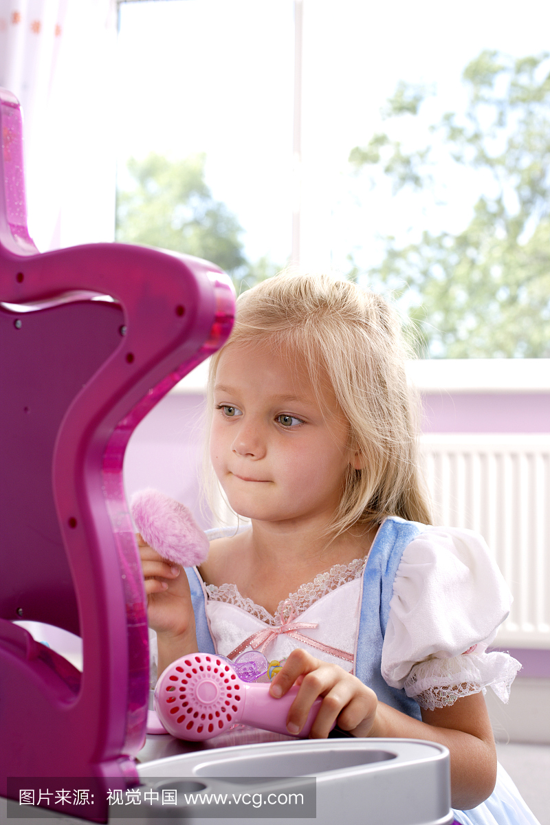 女孩(4-5岁)坐在玩具梳妆台上,看着镜子