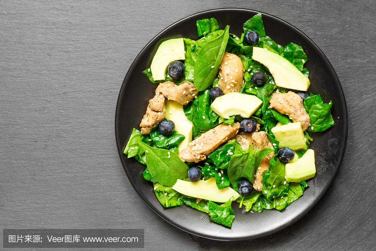 鸡肉沙拉配鳄梨,菠菜和蓝莓在黑色的板块在灰