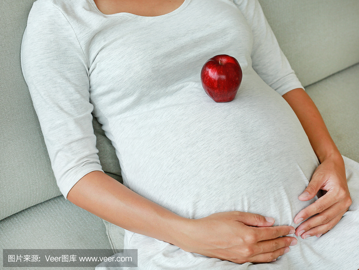 孕妇坐在沙发和地方红苹果果实在她的肚子。