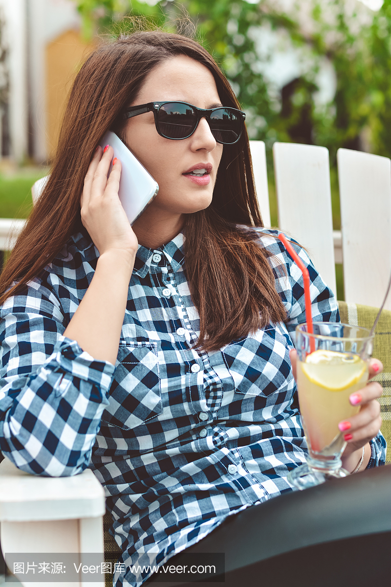 手机和太阳镜喝柠檬水的年轻女子