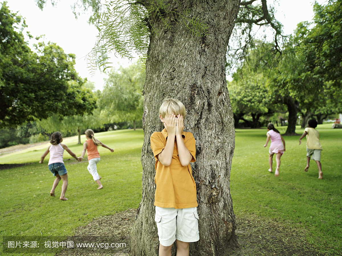 男孩(7-9)用手遮住眼睛玩捉迷藏在公园里,隐藏