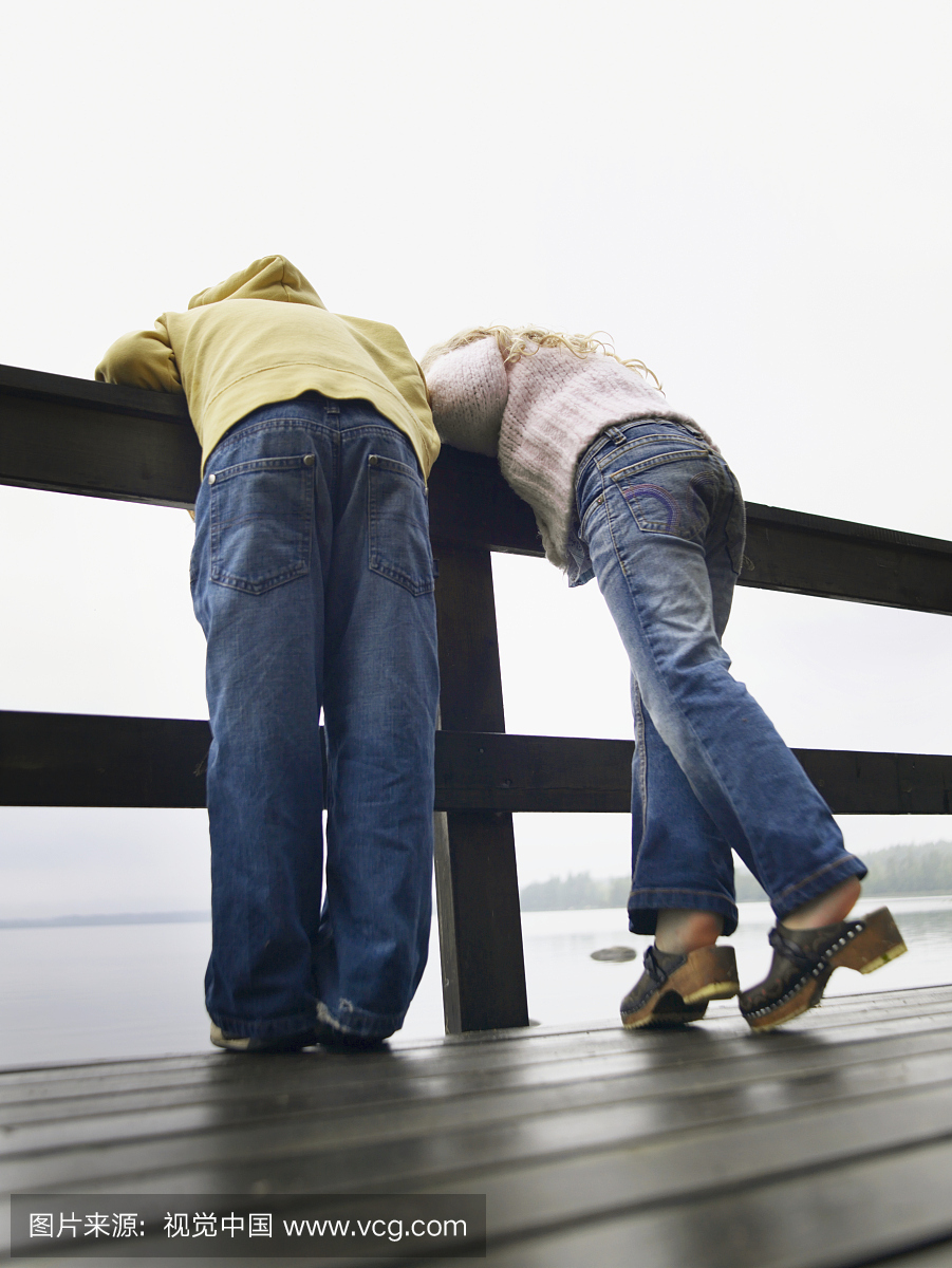 年轻的男孩和女孩靠在湖边的栏杆上。