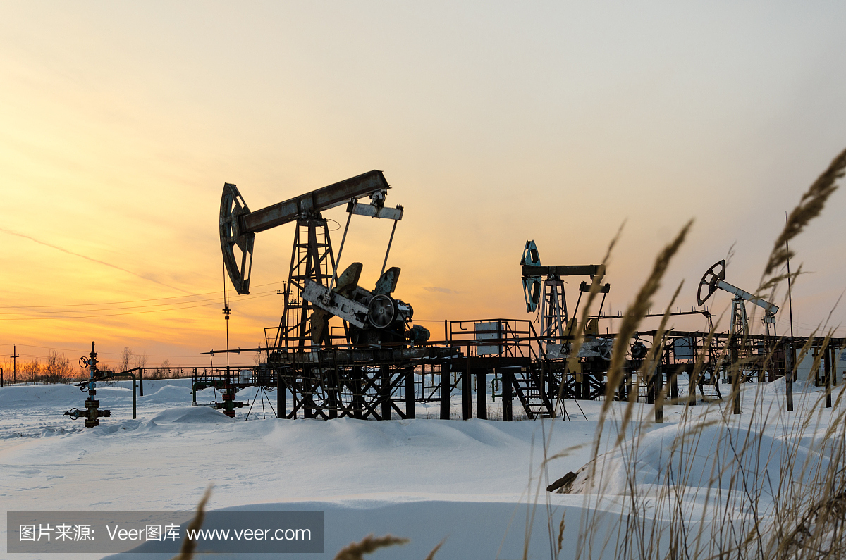 抽油机,井口和管道在日落期间在油田