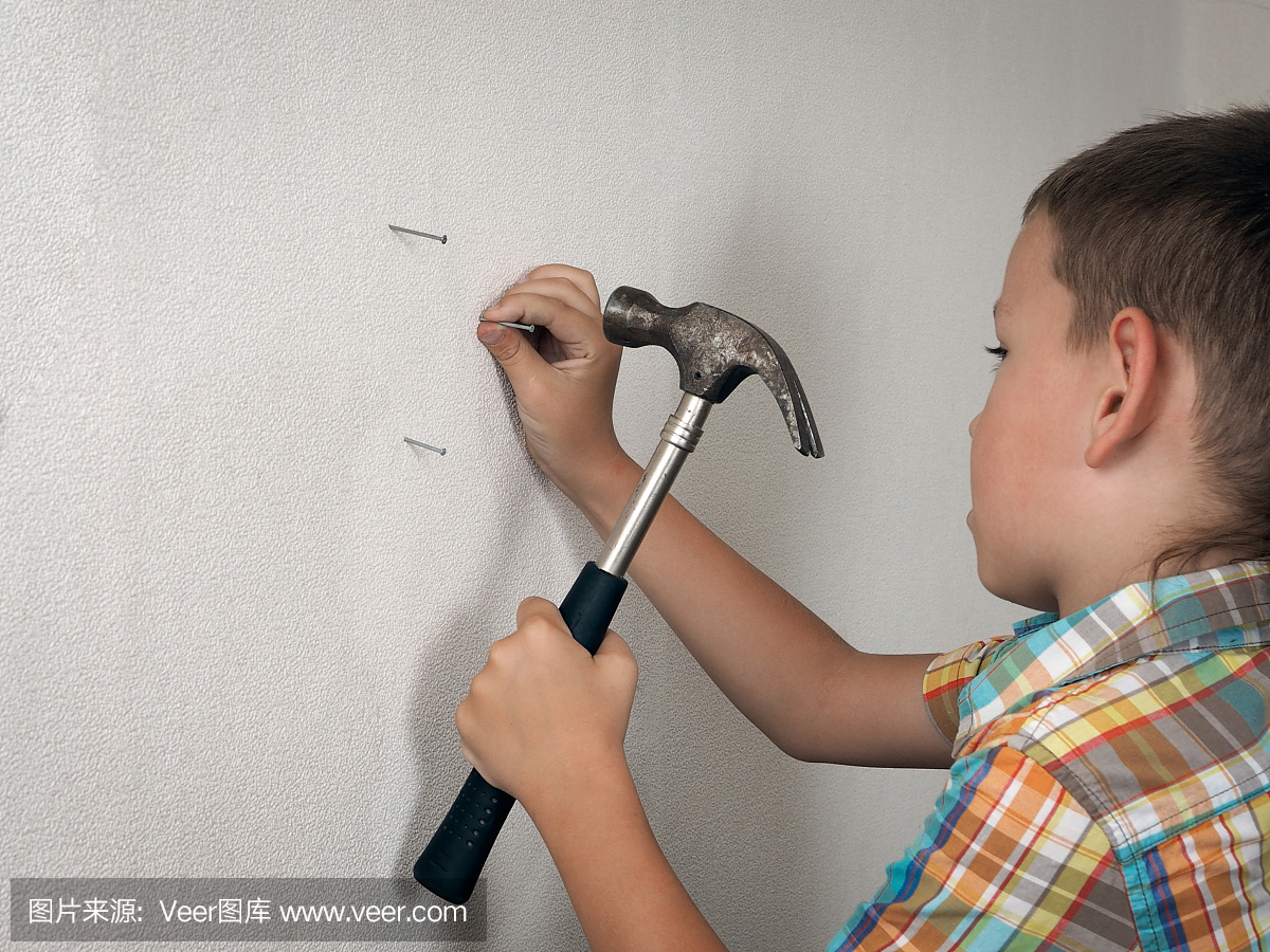 小男孩正在用锤子敲钉在墙上。有趣的孩子6岁
