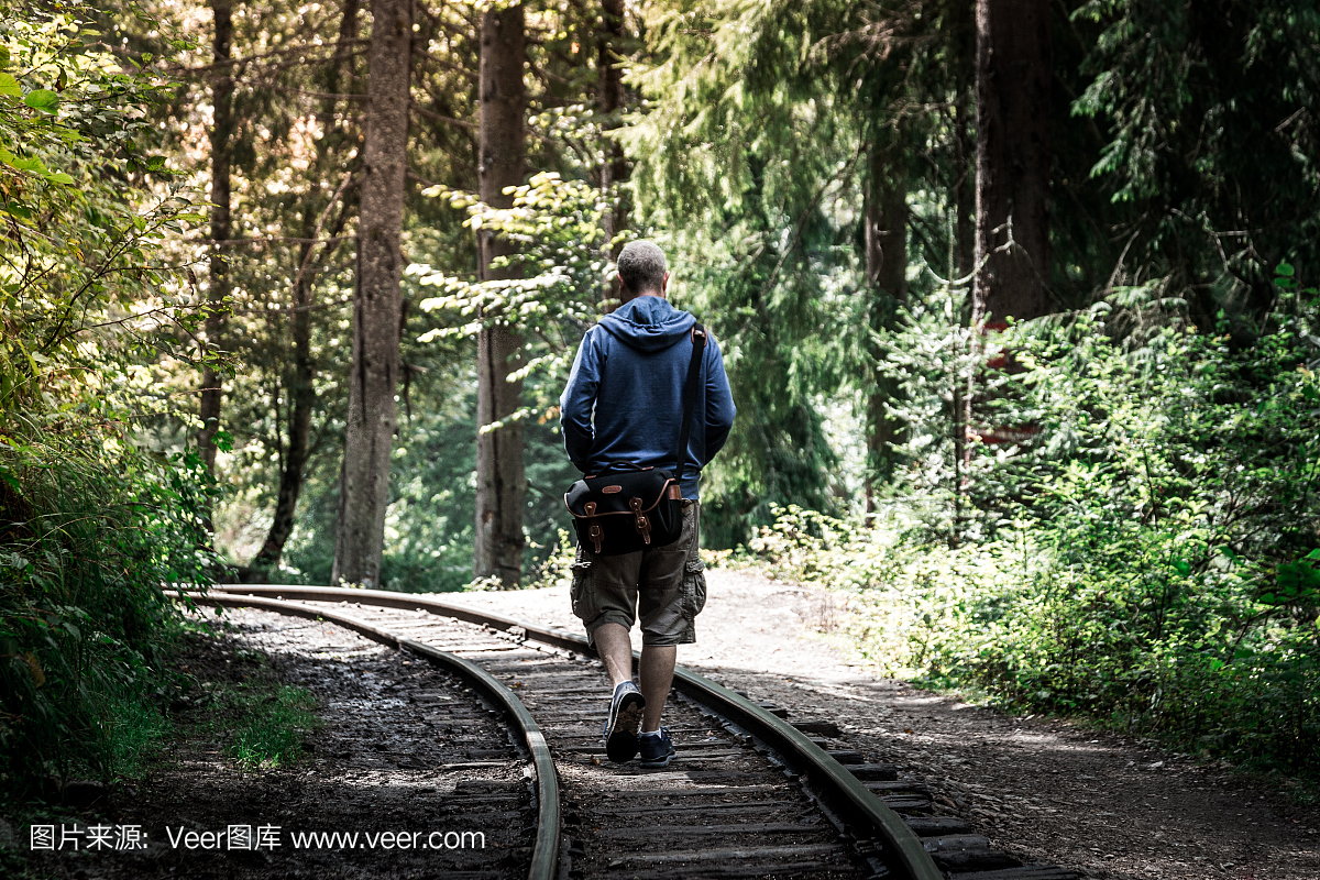 年轻的冒险的人独自走在铁轨上在森林里的背影