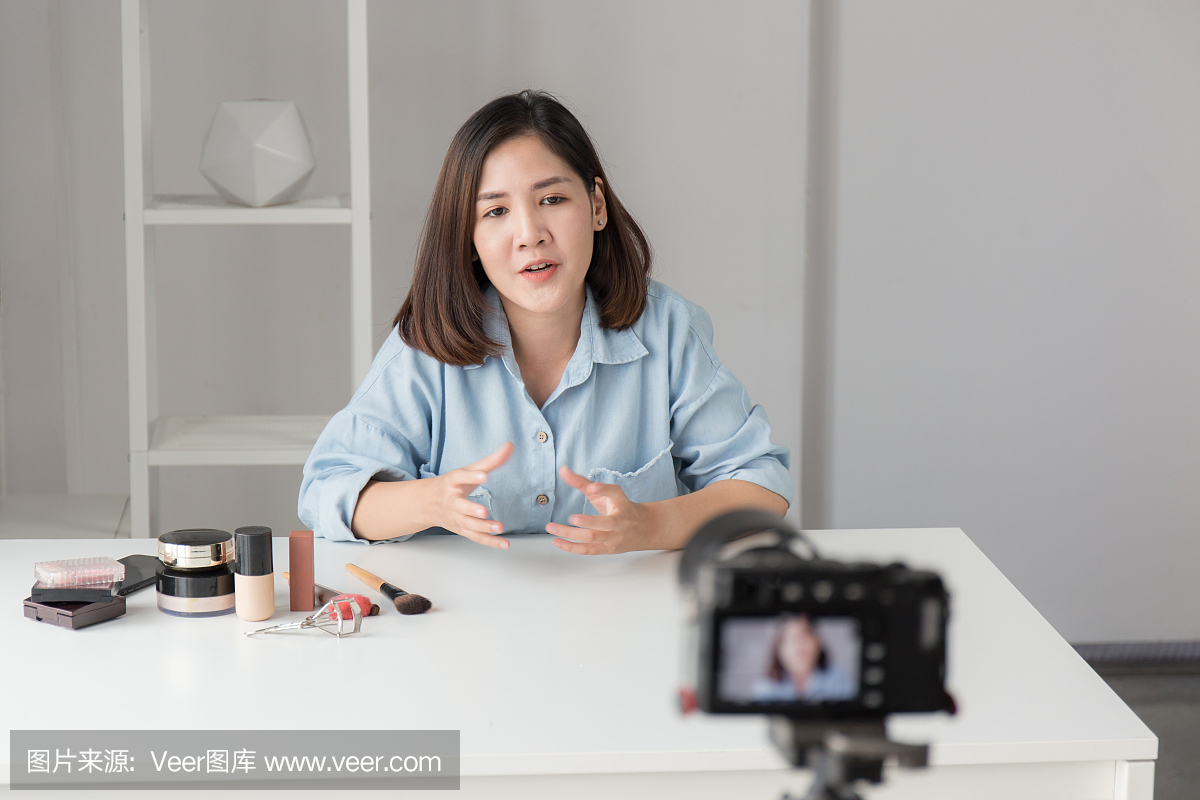亚洲女性正在通过数码相机录像回顾化妆品的在