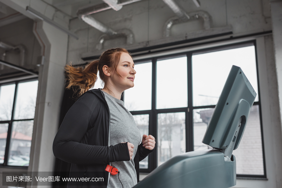 肥胖的女孩在健身房的跑步机上训练