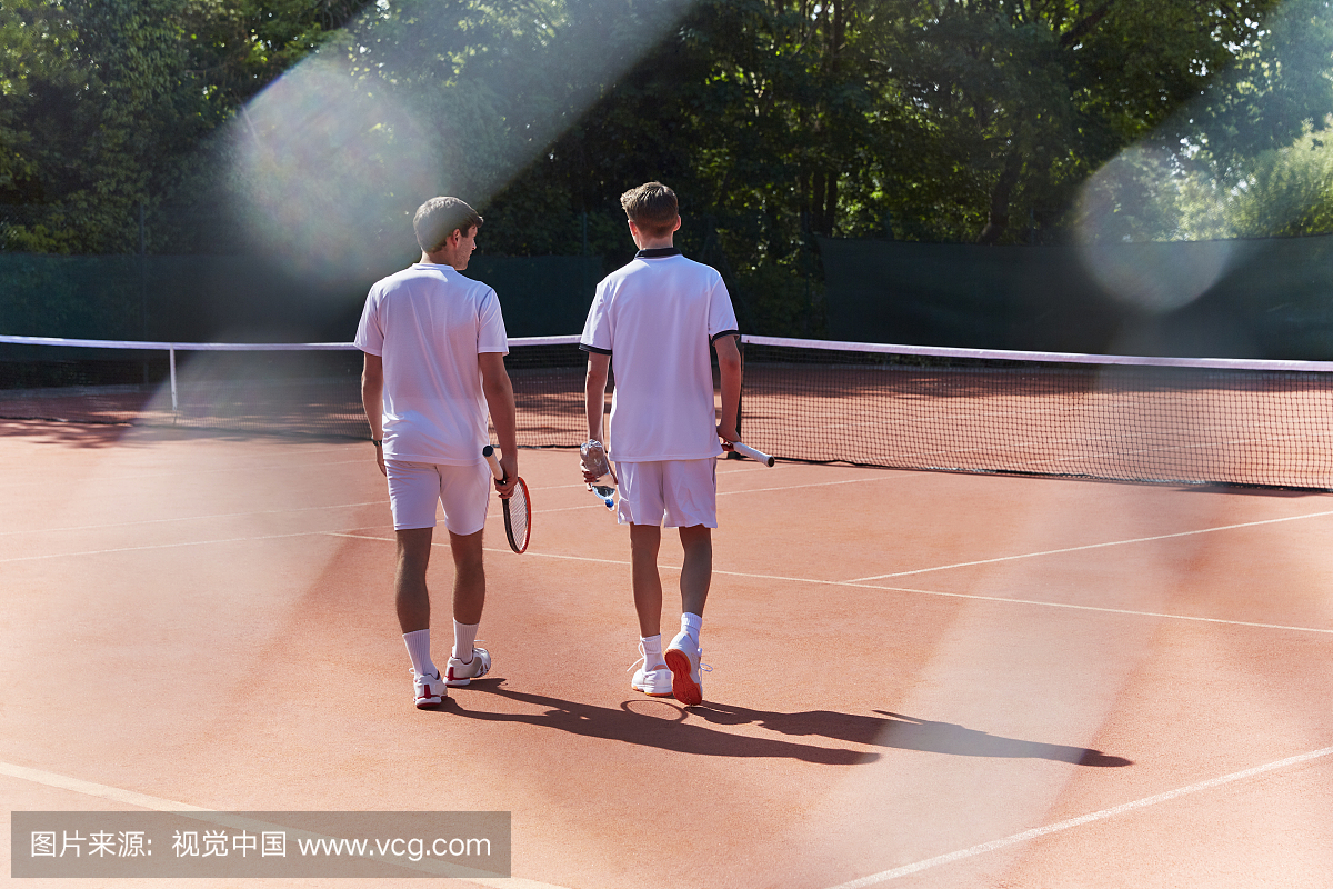 年轻的男网球运动员走在阳光明媚的红土网球场