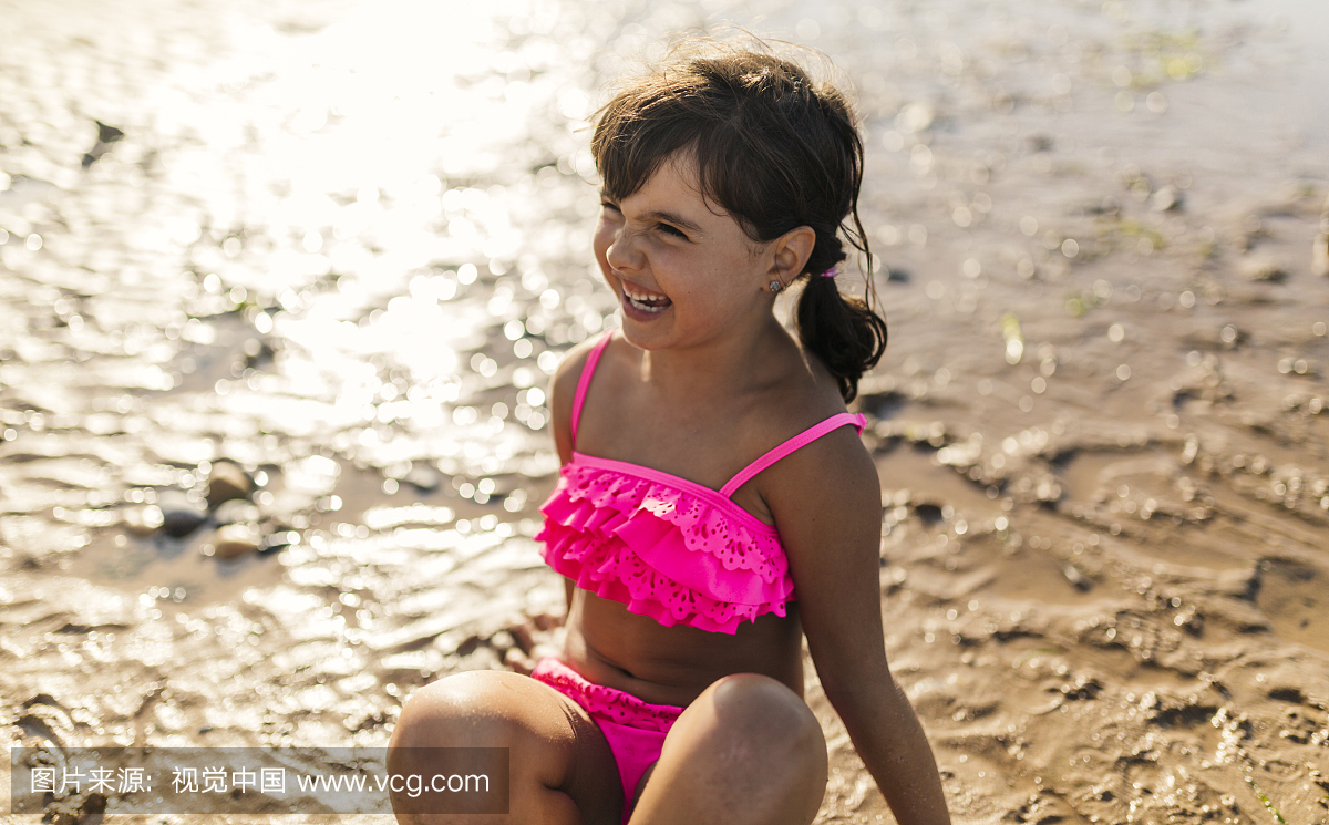 在海滩上穿粉色比基尼泳装的微笑的小女孩的肖