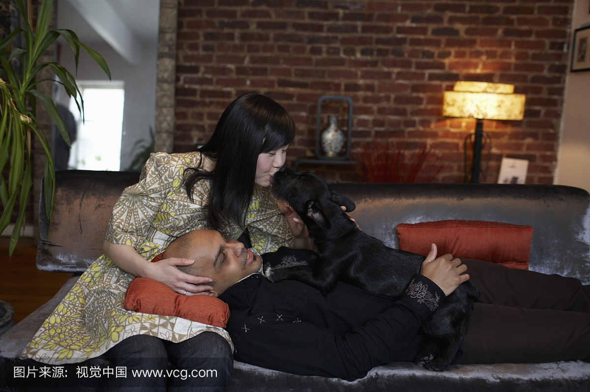 中年成人夫妇在沙发上与狗,女人亲吻狗