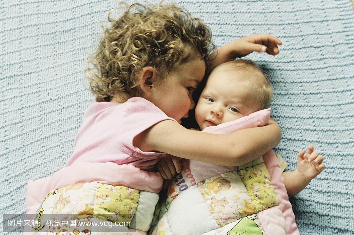 女孩(2-4)拥抱妹妹(0-3个月)在毯子上,俯视图