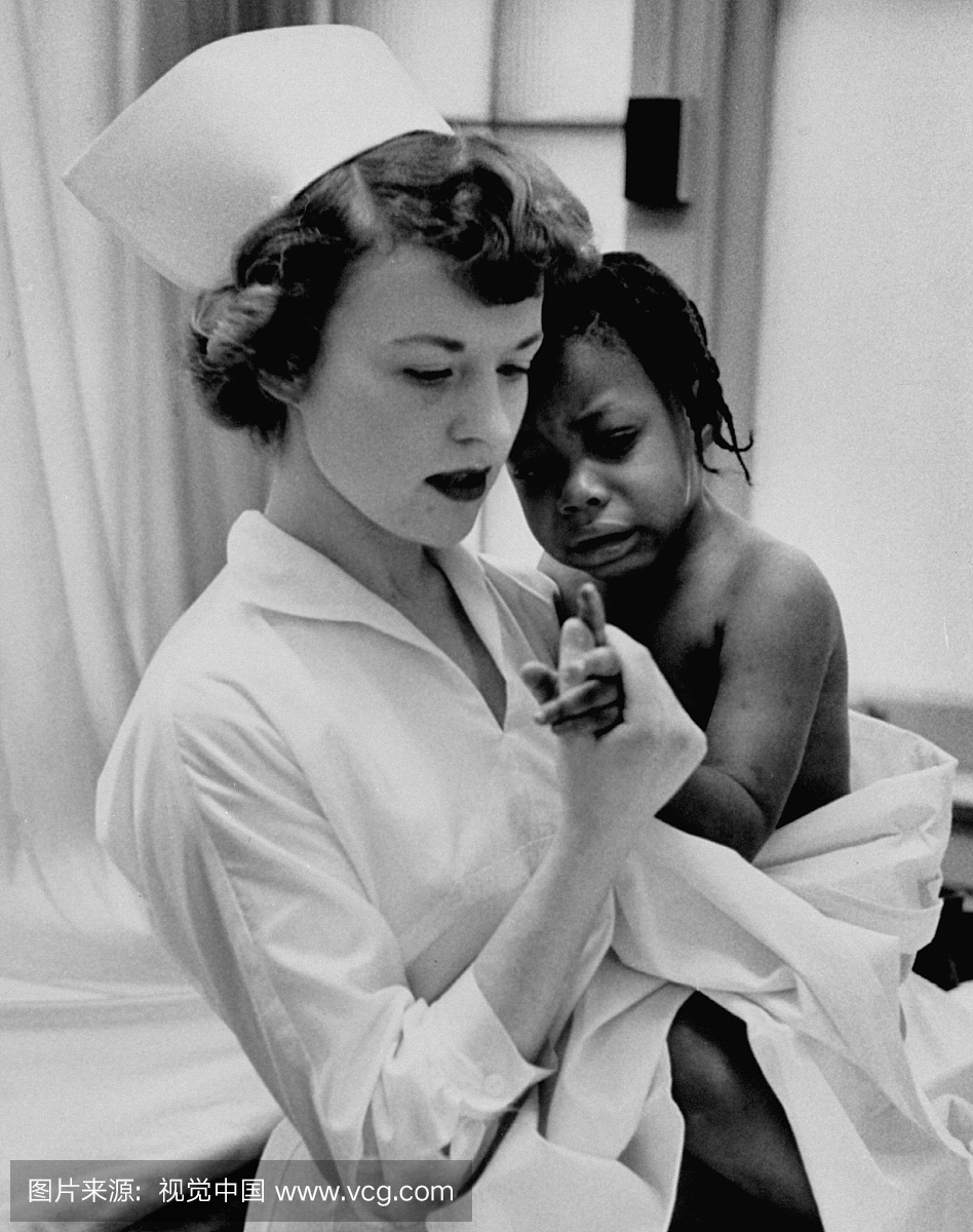 护士握着非裔美国女孩的怀抱,检查她的手指。