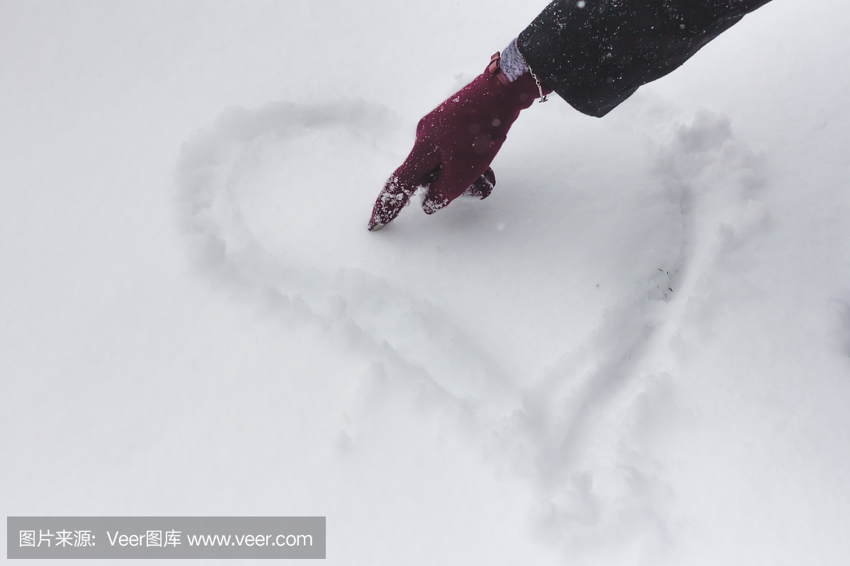 手中的红色手套在雪地上画心。在雪上的心。