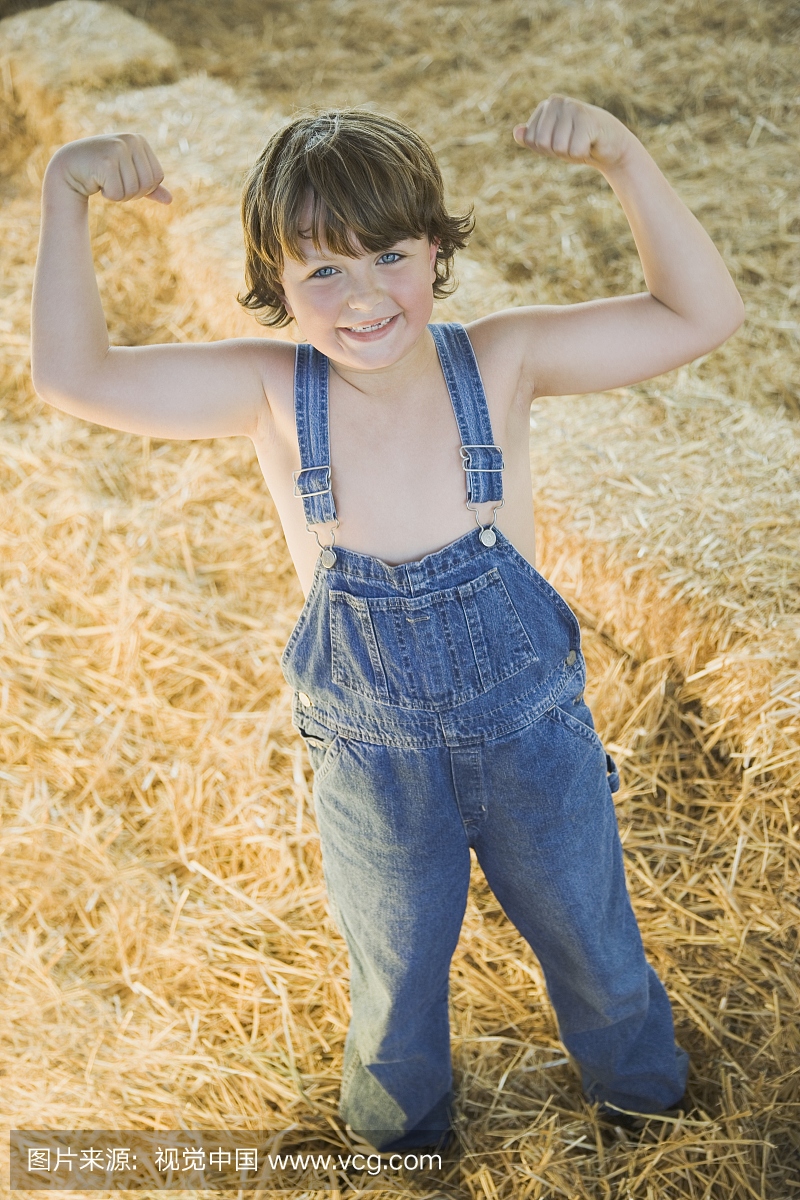 年轻的男孩穿着工作服和弯曲的肌肉在干草