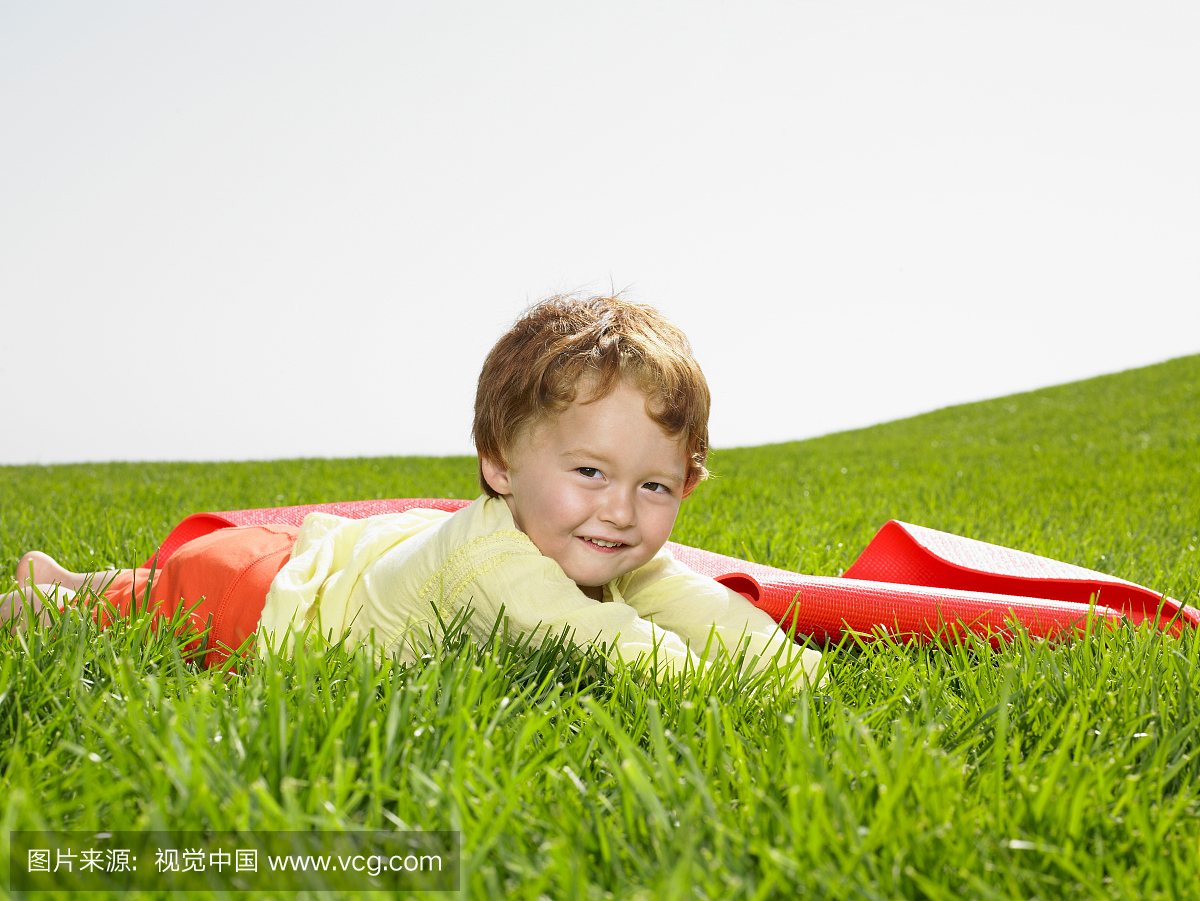 男孩(21-24个月)躺在田野旁边的瑜伽垫,肖像