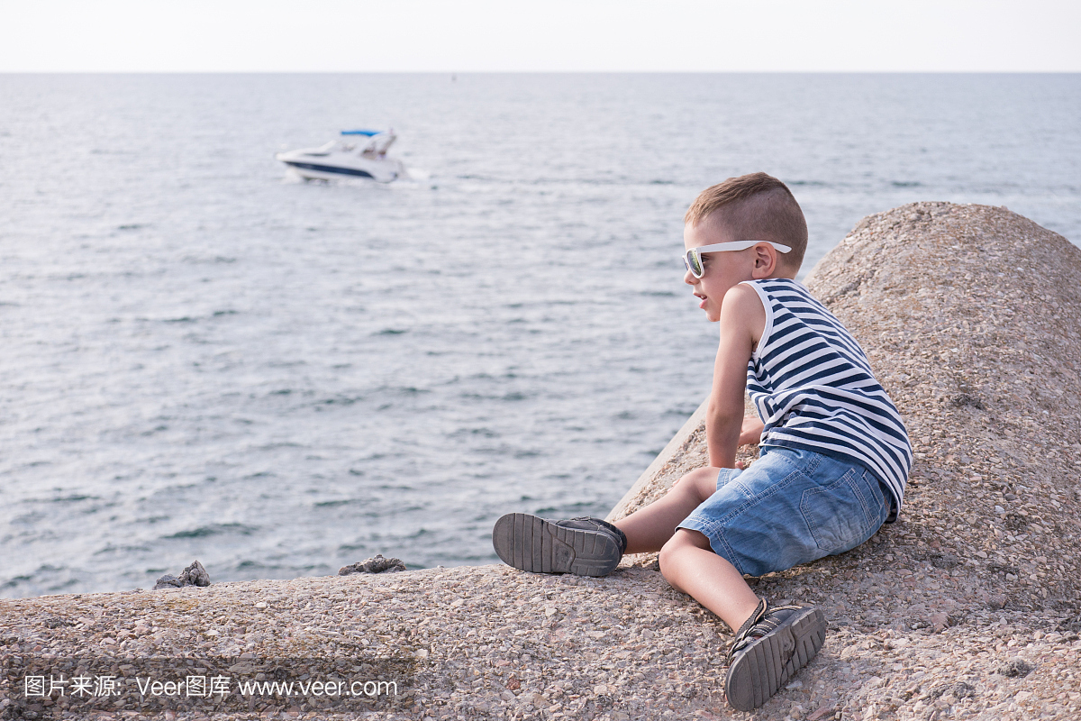 小孩带着太阳眼镜和条纹衬衫在海上与浮船