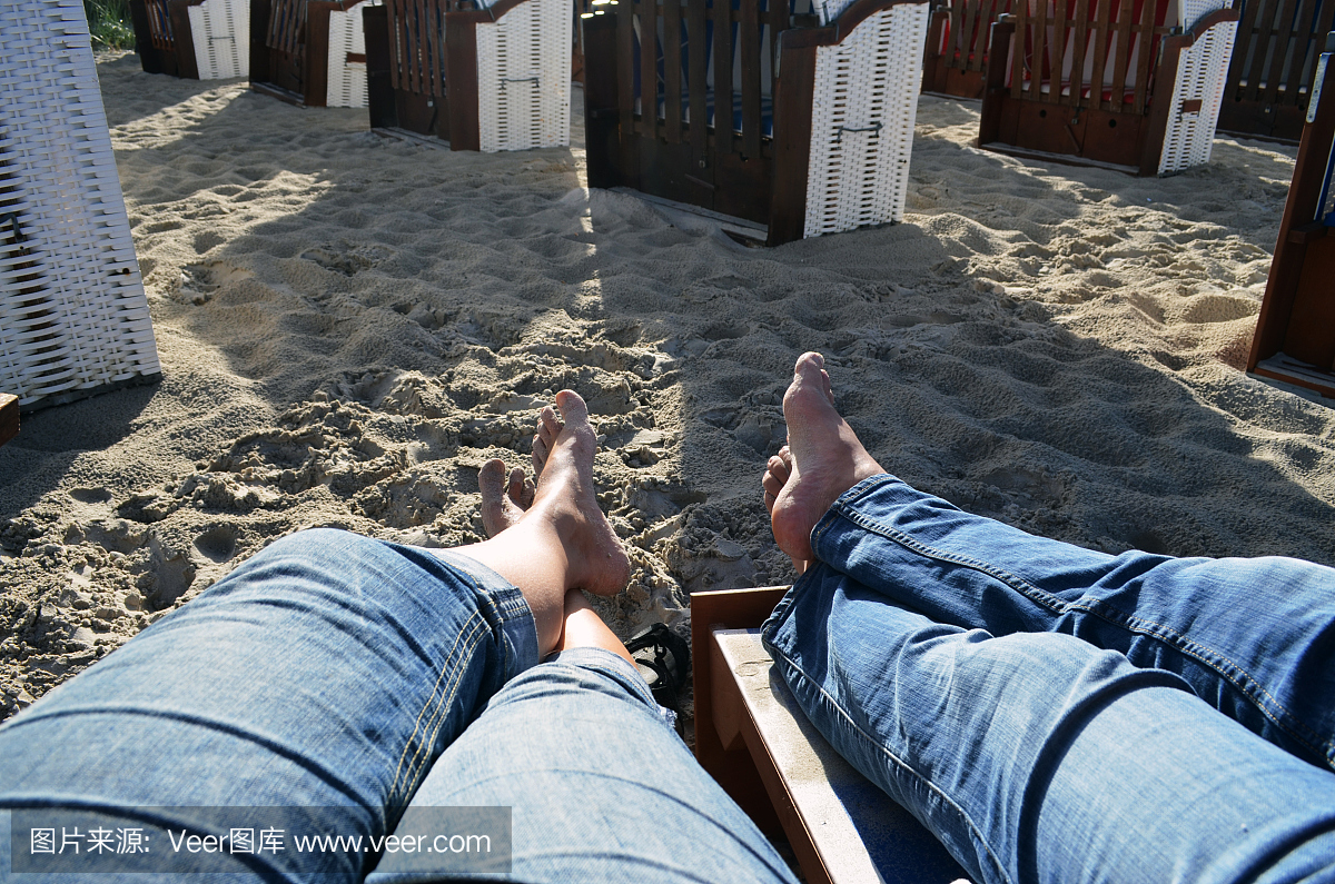 一对夫妇在赤脚坐在沙滩椅上的牛仔裤的腿