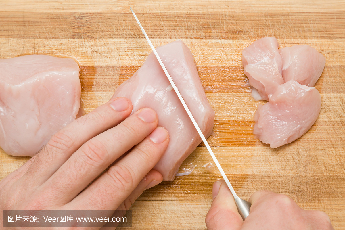 厨师的手用刀在厨房的木板上切割鸡肉。准备烹
