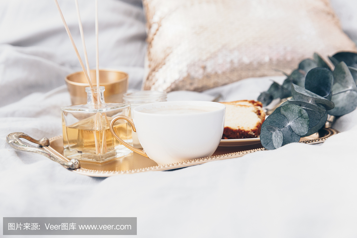 金托盘与咖啡和桉树干净的白色床上用品。早上