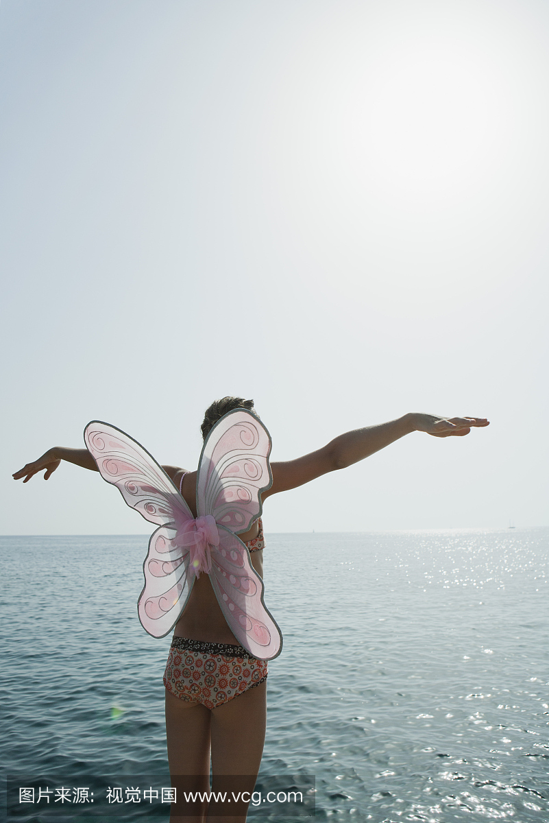 比基尼泳装穿蝴蝶服装的女孩,站在海洋与双臂
