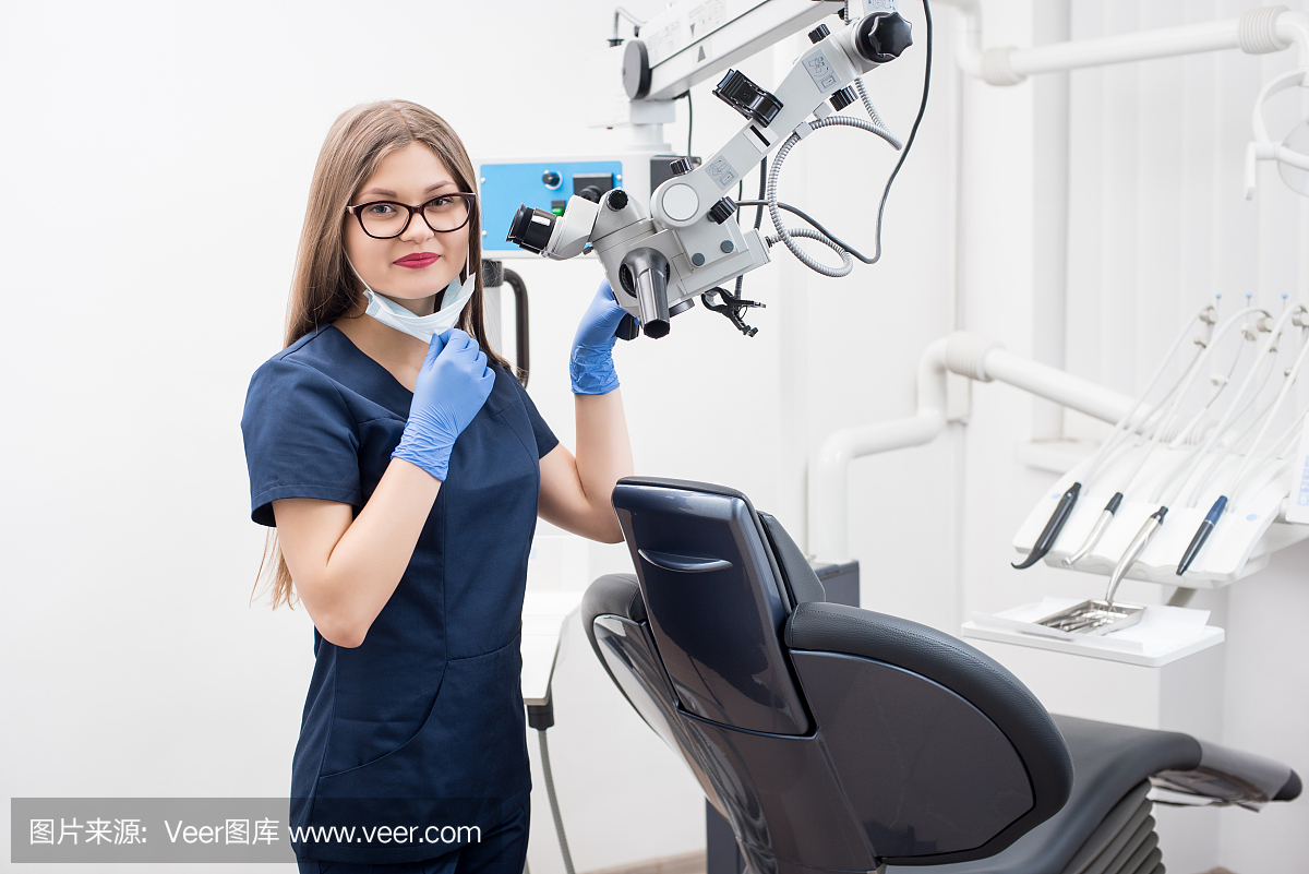美丽的女牙医与显微镜在现代牙科诊所的画像。