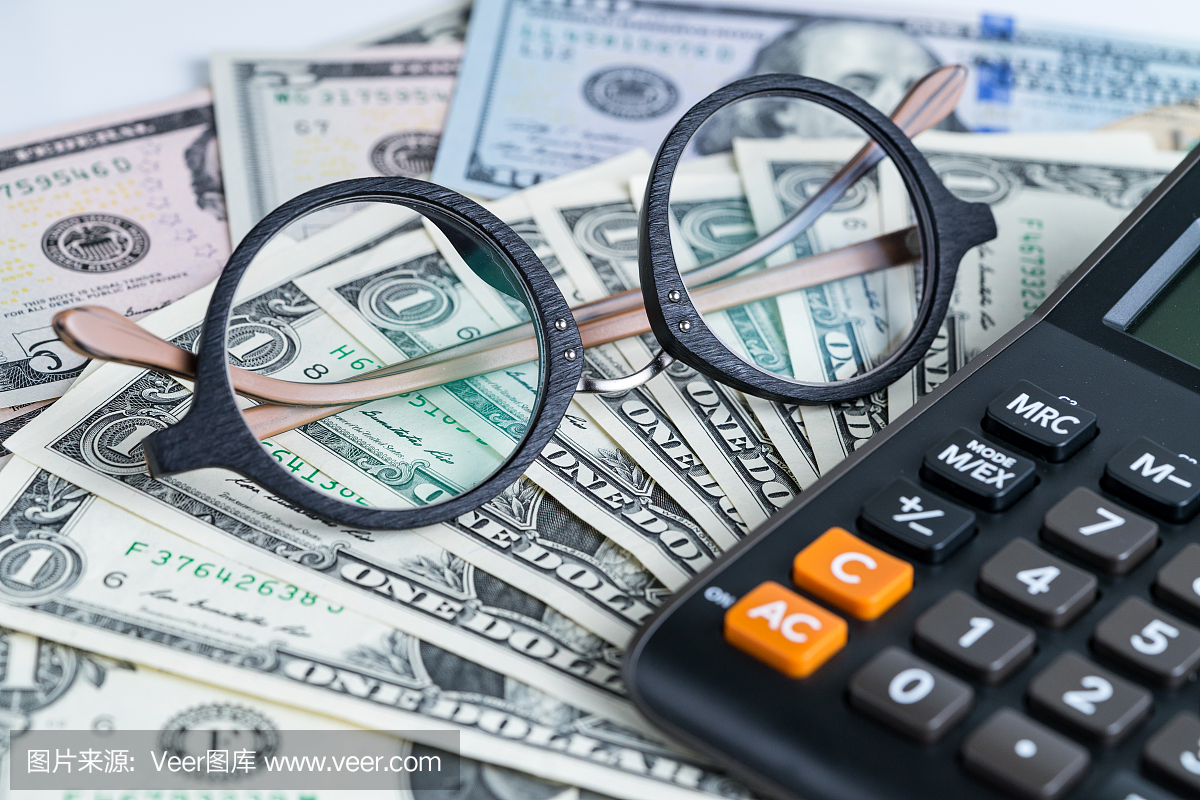 戴着眼镜的企业会计或税计算概念在堆美元钞票
